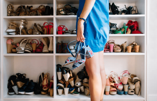 femme devant placard plein de chausures avec une paire de sandales à talons à la main