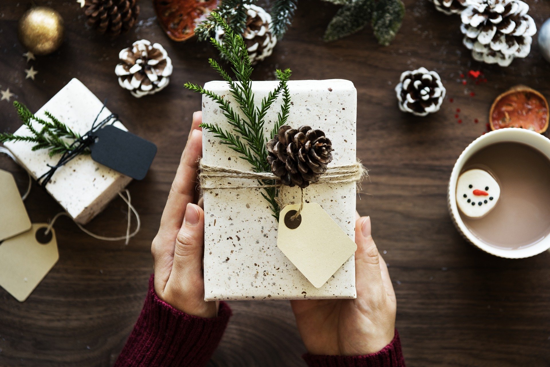 Femme qui tient un paquet cadeau de Noël au-dessus d'une table en bois décorée avec des pommes de pin