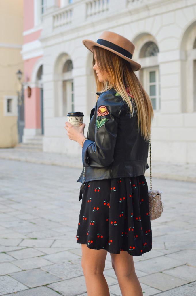 femme blonde portant une veste en cuir avec une fleur sur le bras sur une robe noir imprimé et un chapeau